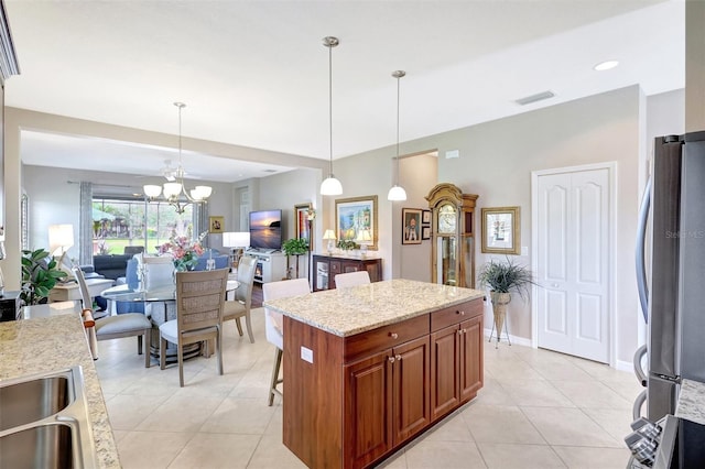 kitchen featuring light tile patterned floors, light stone counters, freestanding refrigerator, brown cabinetry, and decorative light fixtures