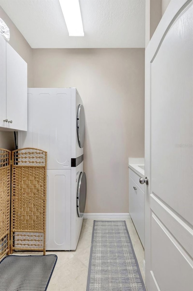 laundry area featuring a textured ceiling, stacked washing maching and dryer, cabinet space, and baseboards