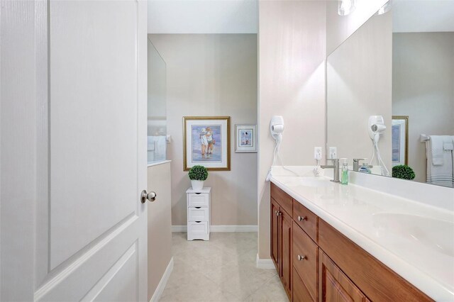 full bathroom with double vanity, tile patterned flooring, baseboards, and a sink