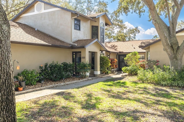 view of front of house featuring a shingled roof, a front lawn, and stucco siding