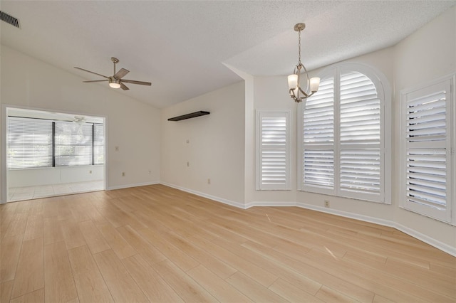 empty room featuring light wood finished floors, visible vents, vaulted ceiling, a textured ceiling, and ceiling fan with notable chandelier