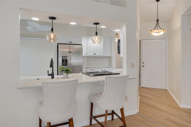 kitchen with tasteful backsplash, stainless steel fridge with ice dispenser, a breakfast bar area, a peninsula, and light wood-type flooring