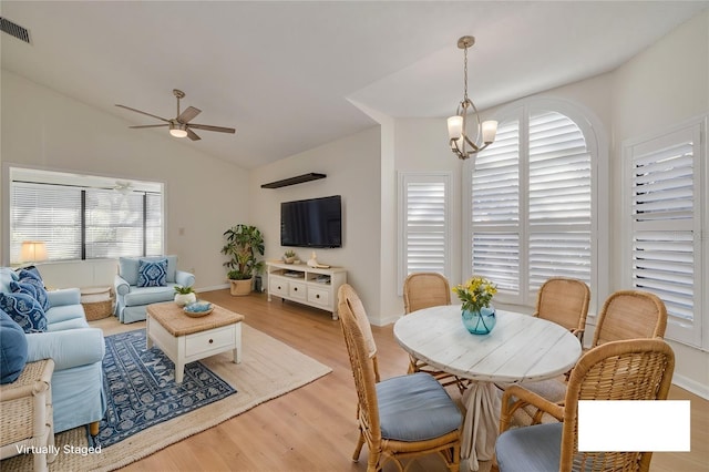 dining space with visible vents, baseboards, lofted ceiling, light wood-style flooring, and ceiling fan with notable chandelier