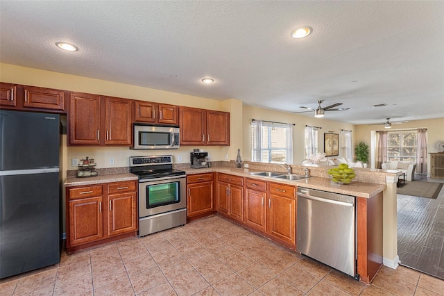 kitchen featuring appliances with stainless steel finishes, brown cabinets, a peninsula, light countertops, and a sink