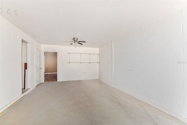 spare room featuring concrete block wall, a ceiling fan, and concrete flooring