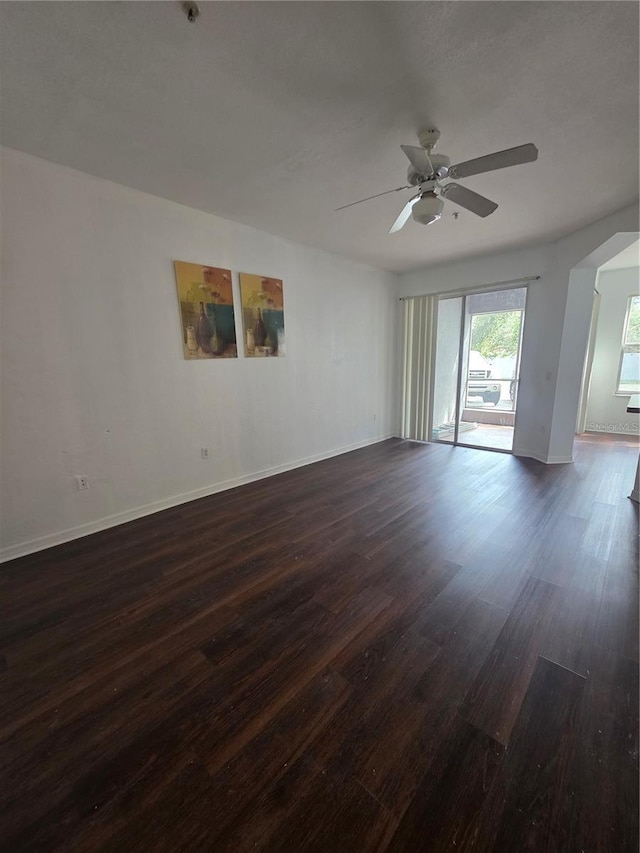 unfurnished room with ceiling fan, baseboards, arched walkways, and dark wood-style flooring