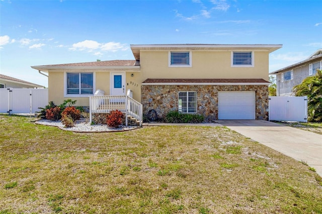 tri-level home with a gate, fence, a front yard, and stucco siding