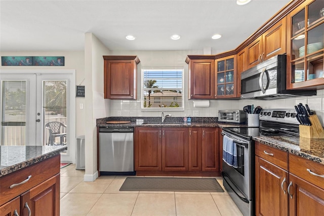 kitchen featuring stainless steel appliances, backsplash, light tile patterned floors, a sink, and dark stone counters