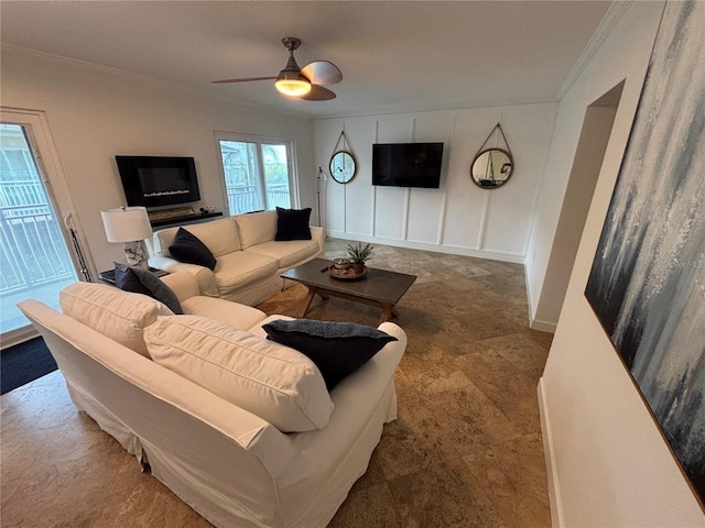 living room with ceiling fan, a decorative wall, baseboards, and crown molding