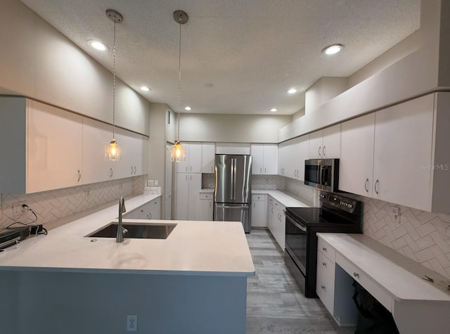 kitchen featuring decorative light fixtures, stainless steel appliances, light countertops, white cabinets, and a sink