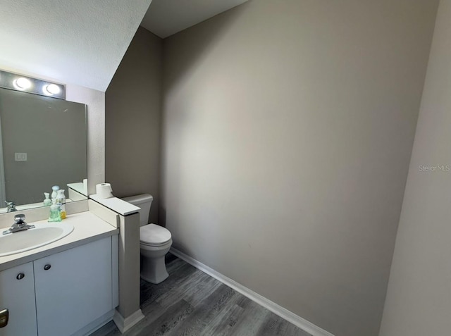 half bath with a textured ceiling, toilet, wood finished floors, vanity, and baseboards