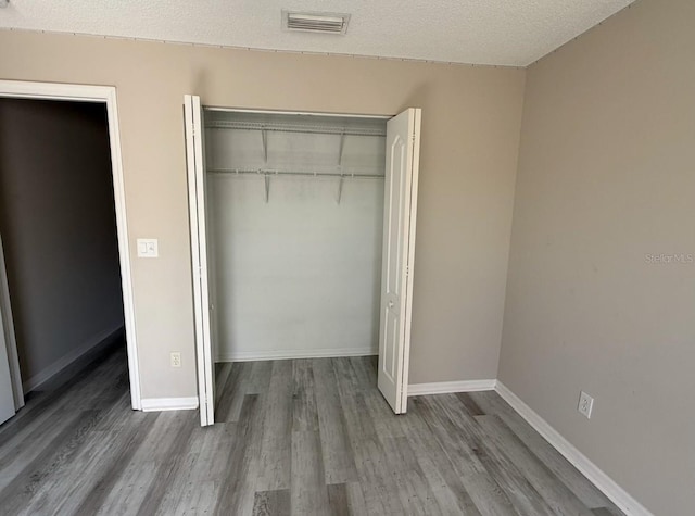 unfurnished bedroom featuring baseboards, visible vents, a closet, and wood finished floors