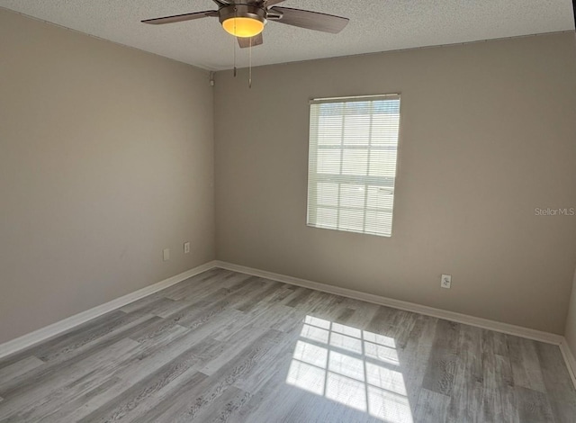 empty room with a textured ceiling, baseboards, a ceiling fan, and light wood-style floors