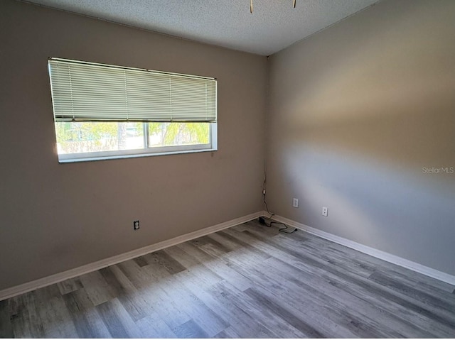 empty room with a textured ceiling, baseboards, and wood finished floors