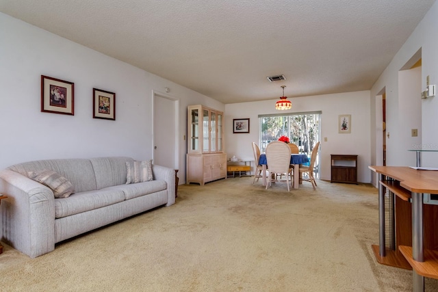 living area featuring visible vents, light colored carpet, and a textured ceiling