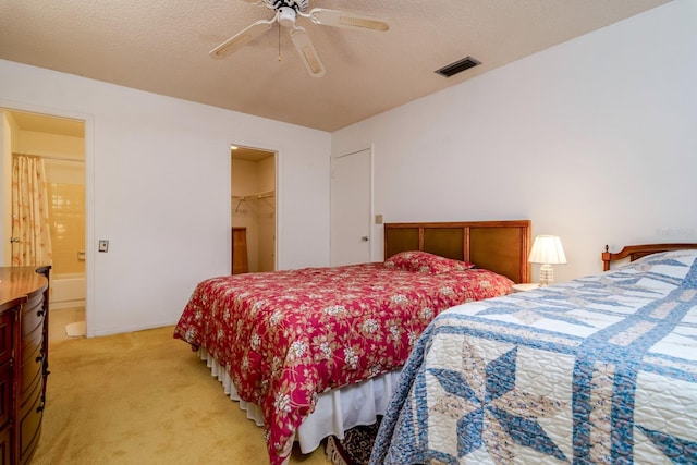 bedroom featuring visible vents, light colored carpet, ceiling fan, a walk in closet, and a textured ceiling