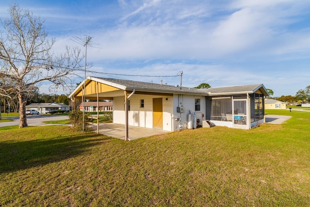 back of house featuring a yard, a carport, a patio area, and a sunroom