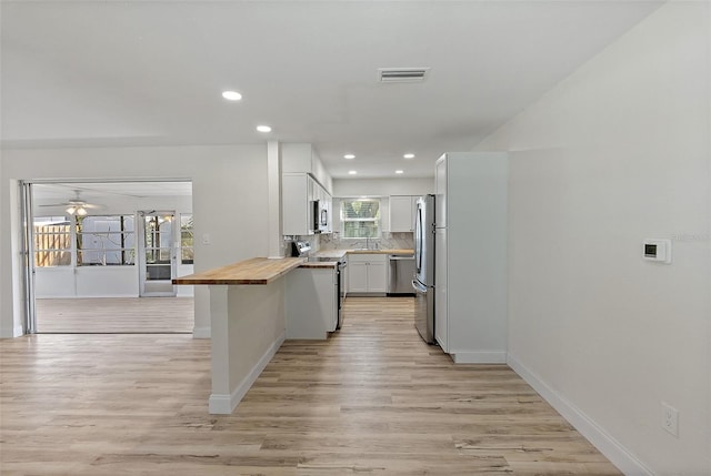 kitchen with stainless steel appliances, a peninsula, white cabinetry, wooden counters, and decorative backsplash