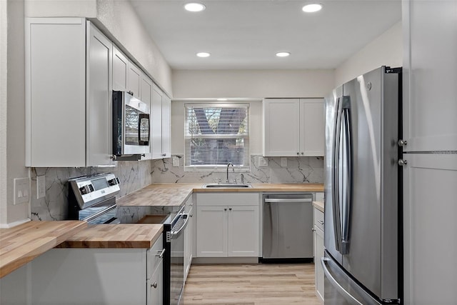 kitchen featuring wood counters, appliances with stainless steel finishes, a sink, light wood-type flooring, and backsplash