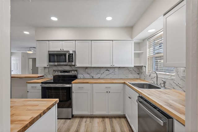 kitchen with decorative backsplash, wood counters, appliances with stainless steel finishes, open shelves, and a sink