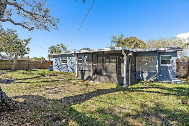 back of house featuring a sunroom, fence, and a lawn