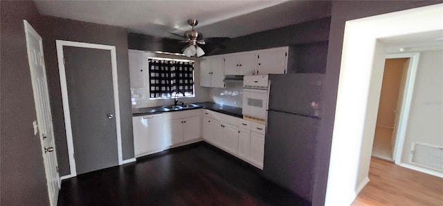 kitchen featuring white appliances, dark countertops, a sink, and white cabinetry