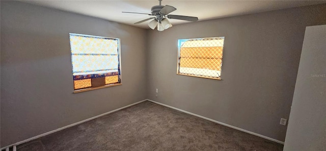 spare room featuring a healthy amount of sunlight, ceiling fan, baseboards, and dark colored carpet