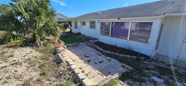 view of side of home with roof with shingles and a patio