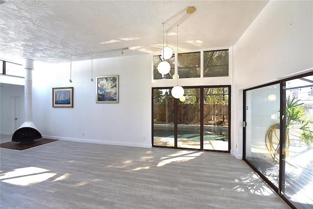 unfurnished living room featuring baseboards, a textured ceiling, a high ceiling, and wood finished floors