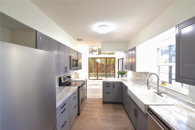 kitchen featuring light stone counters, gray cabinetry, stainless steel appliances, wood finished floors, and a sink