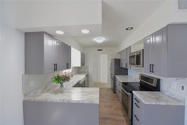 kitchen with stainless steel appliances, a sink, visible vents, gray cabinets, and tasteful backsplash