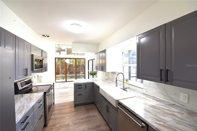 kitchen featuring wood finished floors, light stone countertops, stainless steel appliances, gray cabinetry, and a sink