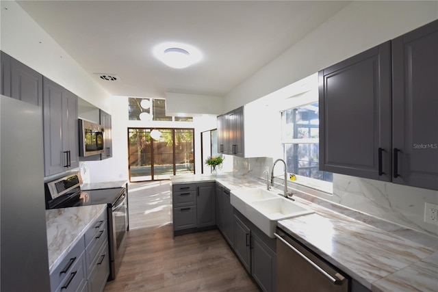 kitchen featuring stainless steel appliances, a sink, gray cabinets, light stone countertops, and tasteful backsplash