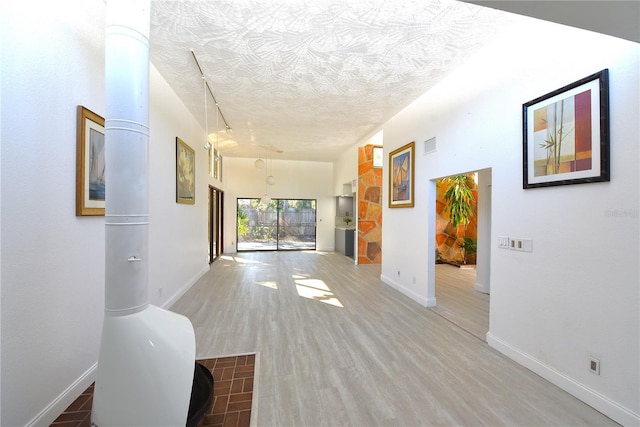 corridor with visible vents, a textured ceiling, baseboards, and wood finished floors