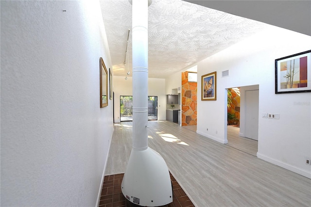 corridor featuring visible vents, a textured wall, a textured ceiling, wood finished floors, and baseboards