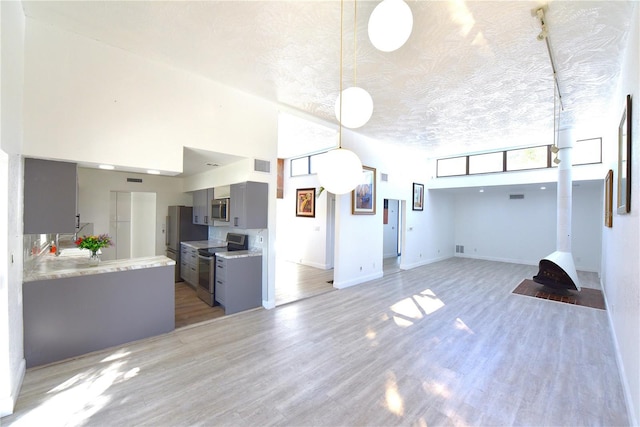 kitchen featuring stainless steel appliances, gray cabinets, light countertops, a high ceiling, and light wood-type flooring