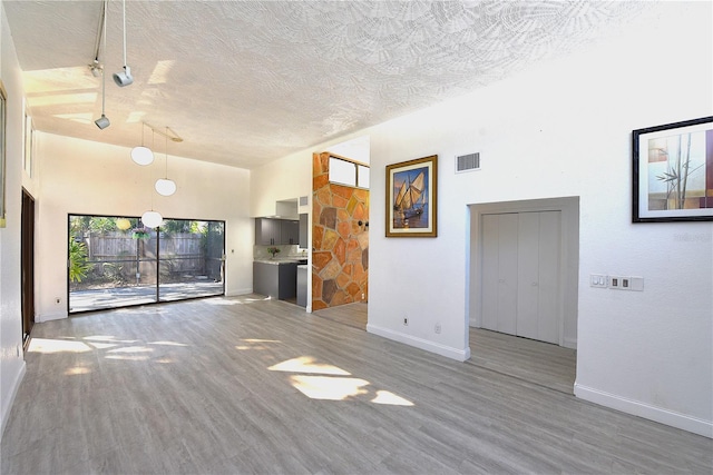 unfurnished living room featuring baseboards, visible vents, a towering ceiling, wood finished floors, and a textured ceiling