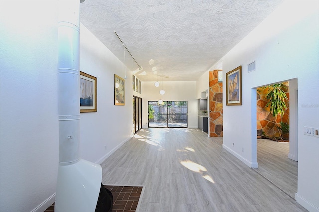 hall with visible vents, a textured ceiling, baseboards, and wood finished floors