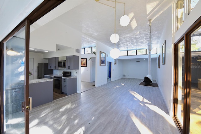 unfurnished living room with light wood-type flooring, visible vents, a high ceiling, and baseboards