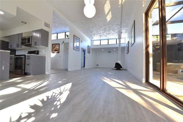 unfurnished living room with light wood finished floors, baseboards, a high ceiling, and visible vents