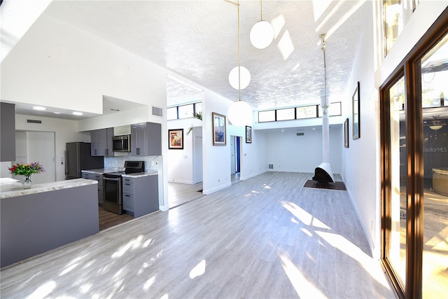 kitchen featuring light wood finished floors, a towering ceiling, gray cabinets, stainless steel appliances, and light countertops