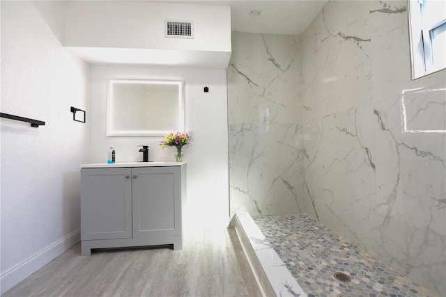 bathroom with a marble finish shower, visible vents, vanity, wood finished floors, and baseboards