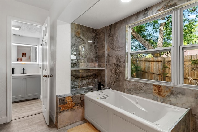 full bath featuring a whirlpool tub, vanity, a textured ceiling, and wood finished floors