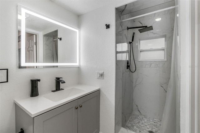 bathroom featuring a marble finish shower, vanity, and a textured wall