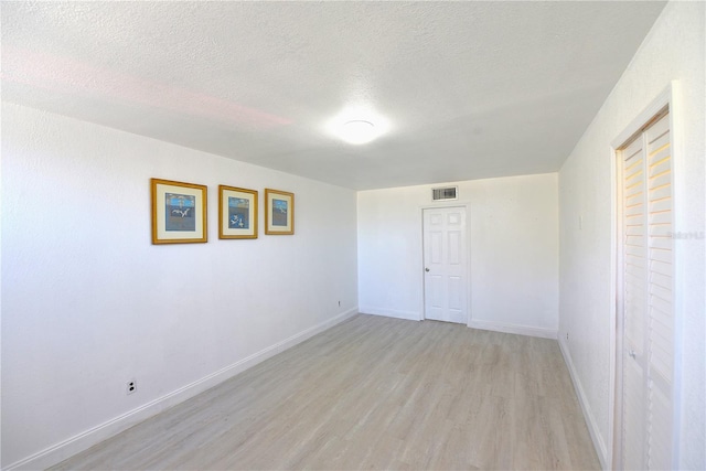 spare room featuring light wood-type flooring, visible vents, a textured ceiling, and baseboards