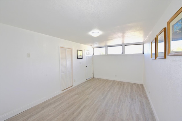 spare room featuring a textured ceiling, light wood-type flooring, and baseboards