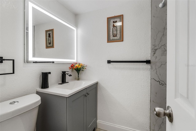 bathroom with a textured wall, vanity, and toilet