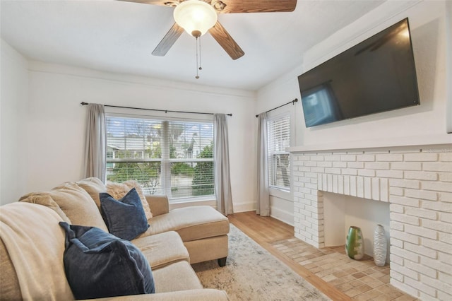 living room featuring light wood finished floors, a fireplace, a ceiling fan, and baseboards