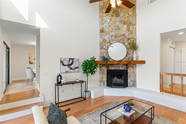 living area with a high ceiling, wood finished floors, and a stone fireplace