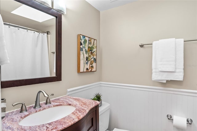 full bath with a skylight, a wainscoted wall, vanity, and toilet